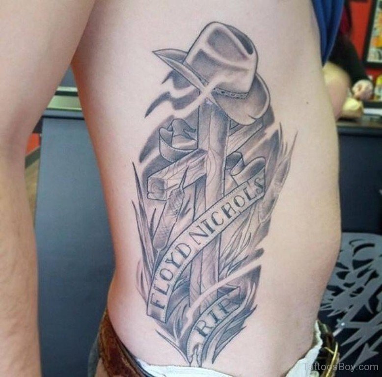 Grey Ink Cross With Cowboy Hat Tattoo On Rib